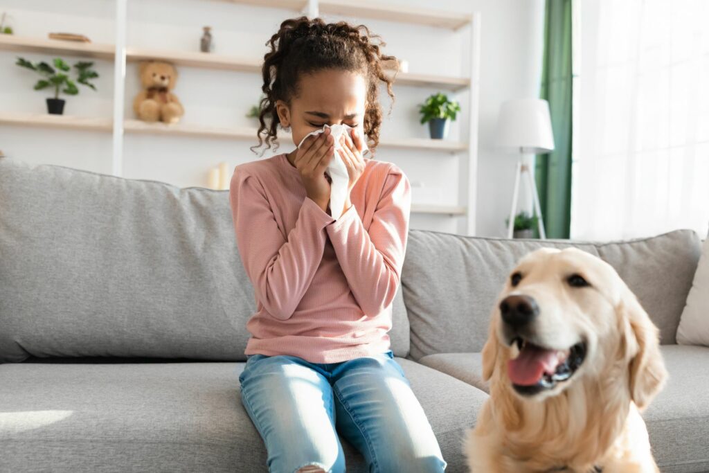 little girl sitting on couch with dog blowing nose
