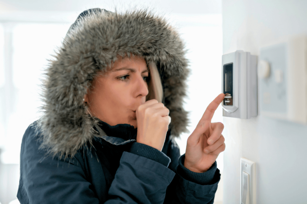 woman wearing coat indoors adjusting thermostat